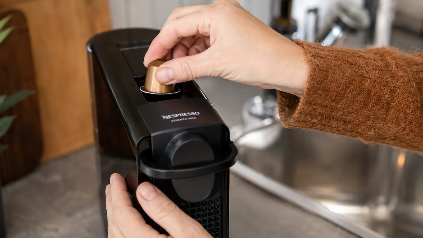 Hand inserting a Nespresso pod into the top of the Essenza Mini machine